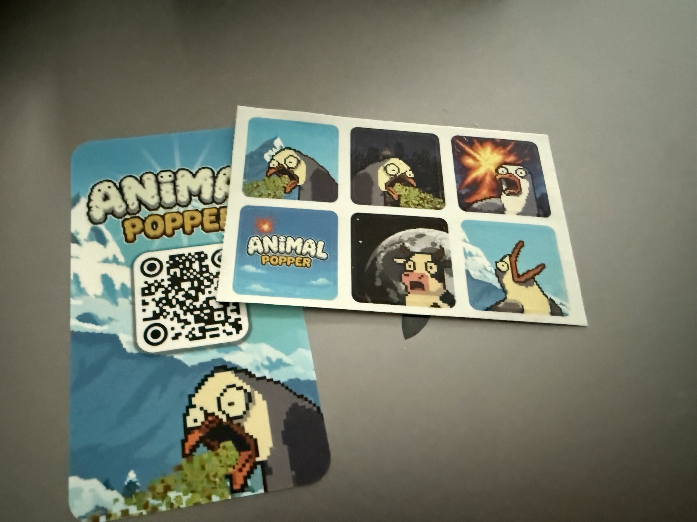 Animal Popper souvenir card with a QR code, beside a sheet of pixel-art animal stickers